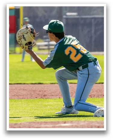 A baseball player in a green and yellow uniform is kneeling on the ground with a baseball glove on his hand. Description generated by AI