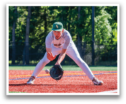 A baseball player in a white and green uniform is bending over to catch a ball. Description generated by AI