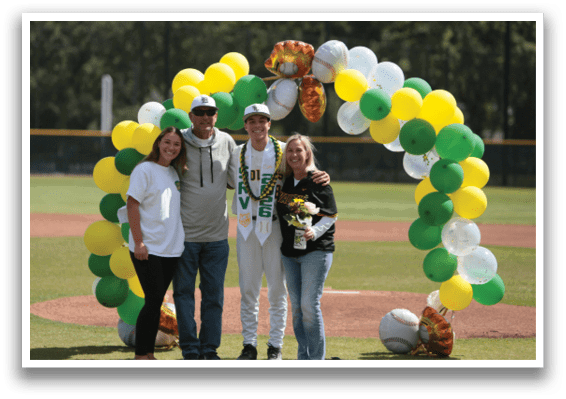 A group of people standing in front of a baseball field with a green and yellow arch. Description generated by AI