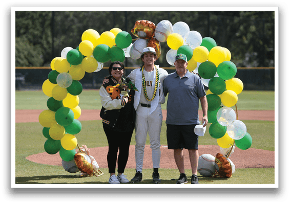 A man and woman stand in front of a baseball field with a green and yellow arch. Description generated by AI