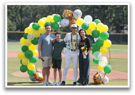 A group of people standing on a baseball field with a green and yellow banner. Description generated by AI