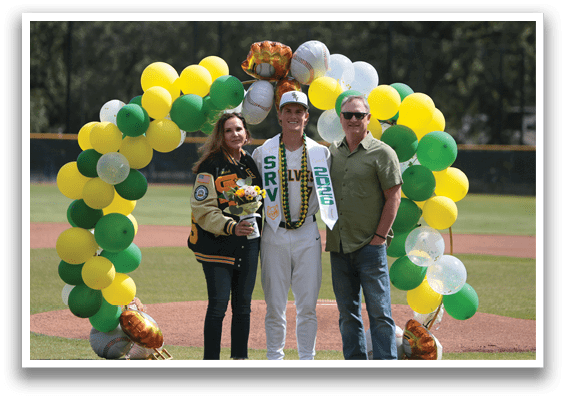 A man and woman are standing in front of a baseball field with a green and yellow arch. Description generated by AI