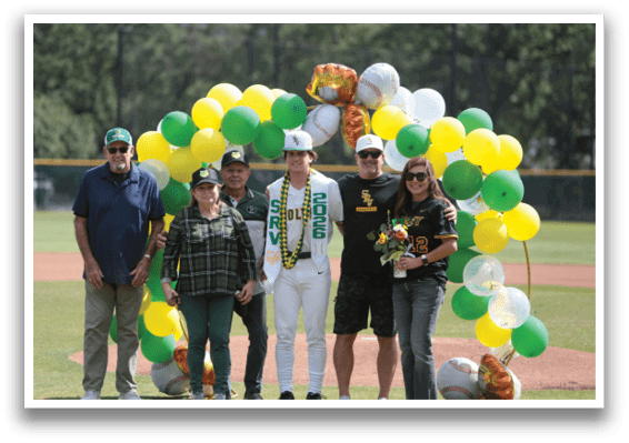 A group of people standing on a baseball field with balloons and flowers. Description generated by AI