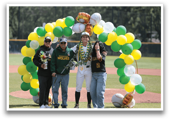 A group of people standing in front of a baseball field with a green and yellow arch. Description generated by AI