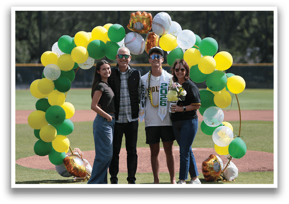A group of people standing in front of a baseball field with balloons and a baseball glove. Description generated by AI