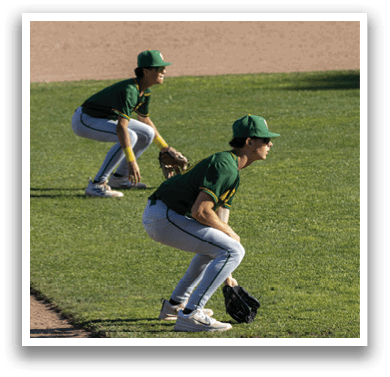 Two baseball players in green and yellow uniforms are crouching on a baseball field. Description generated by AI