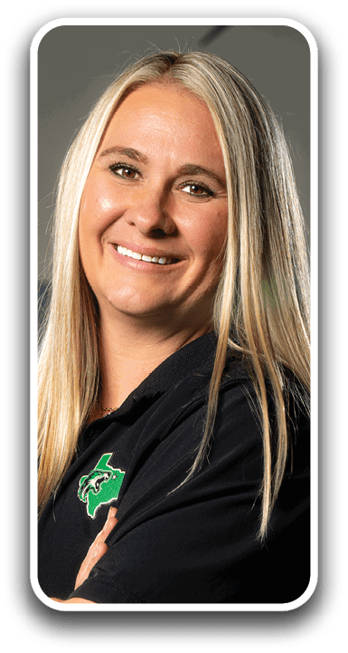 A woman with blonde hair and a green pin on her shirt is standing with her arms crossed. Contenido generado con IA