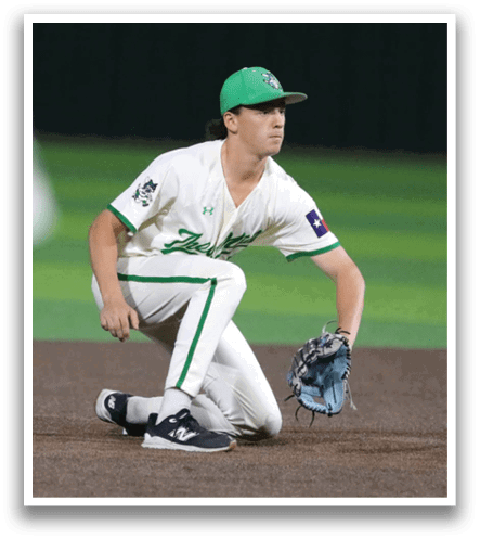 A baseball player is kneeling on the field, wearing a green hat and white uniform. Contenido generado con IA