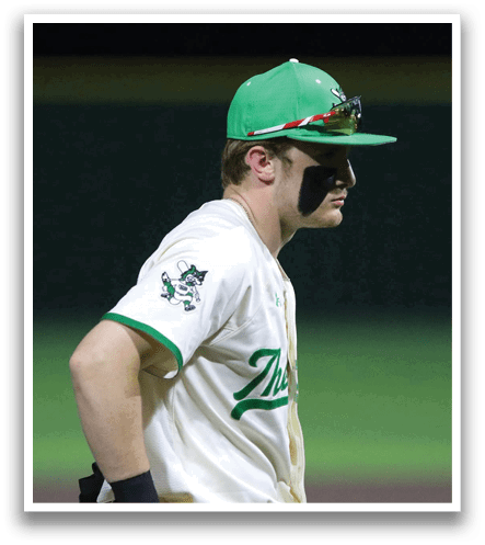 A baseball player wearing a green hat and white uniform walks on the field. Contenido generado con IA