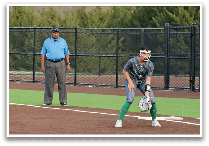 A woman in a grey shirt and green shorts is playing softball. Contenido generado con IA