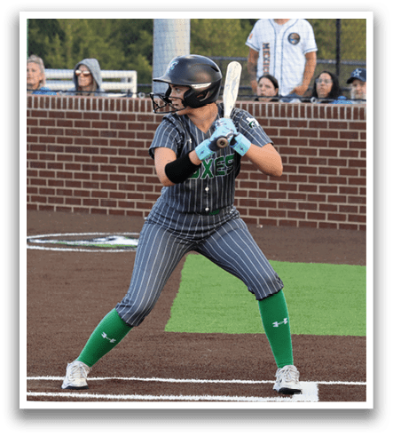 A female baseball player in a grey and black uniform is swinging a bat at a ball. Contenido generado con IA