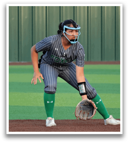 A female baseball player in a green and white uniform is crouching on the field, wearing a helmet and holding a baseball glove. Contenido generado con IA