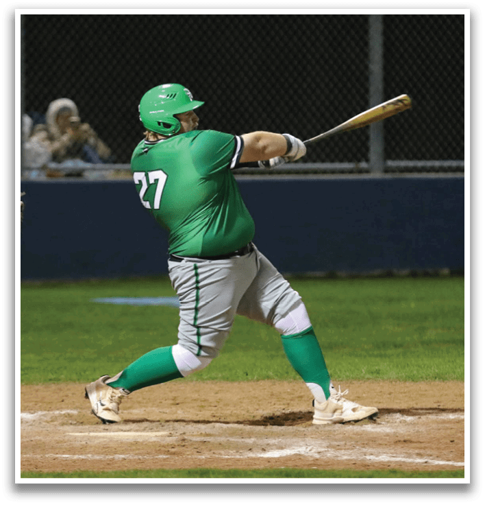 A baseball player in a green shirt and white pants is swinging a bat at a ball. Contenido generado con IA