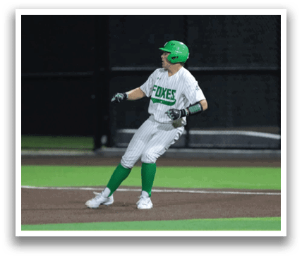 A baseball player in a green shirt and white pants is running towards first base. Contenido generado con IA