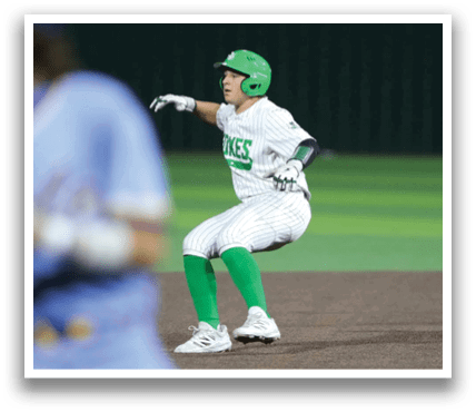 A baseball player in a blue uniform is running towards a base while another player in a green uniform is kneeling down. Contenido generado con IA