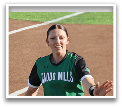A female baseball player wearing a green and black uniform is walking on the field. Contenido generado con IA
