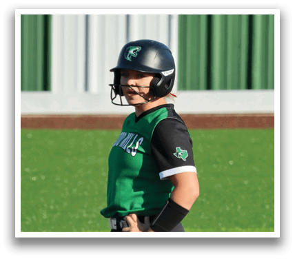 A woman wearing a black and green shirt and a helmet stands on a baseball field. Contenido generado con IA