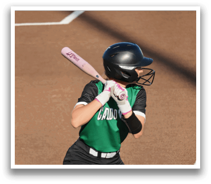 A female baseball player in a green shirt and black pants is holding a bat and preparing to swing. Contenido generado con IA