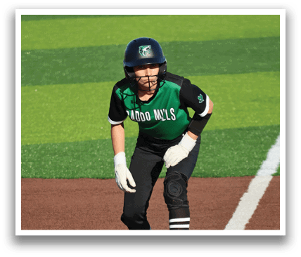 A female baseball player is running towards home plate, wearing a green and black uniform. Contenido generado con IA
