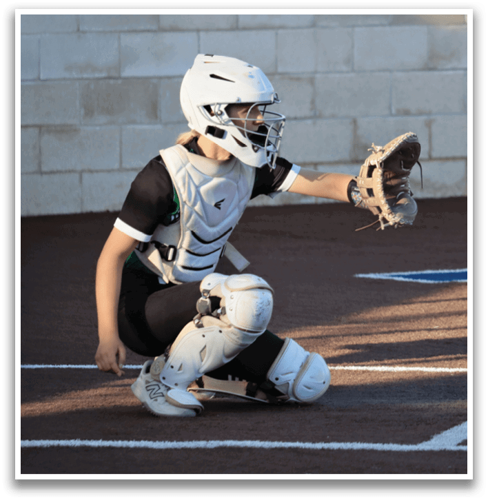 A female baseball player in a catcher's position, wearing a helmet and catcher's mitt, is ready to catch a ball. Contenido generado con IA