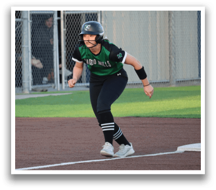 A female baseball player wearing a green and black uniform is running towards home plate. Contenido generado con IA