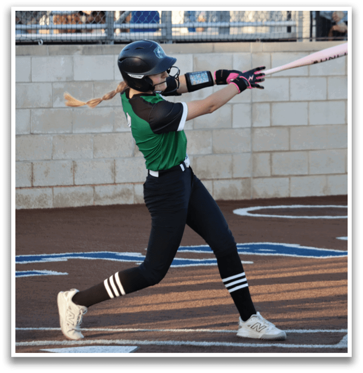 A girl is swinging a bat at a ball, wearing a green and black uniform. Contenido generado con IA