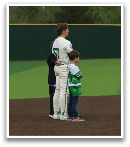 A man and a boy stand on a baseball field, both wearing white uniforms. Contenido generado con IA