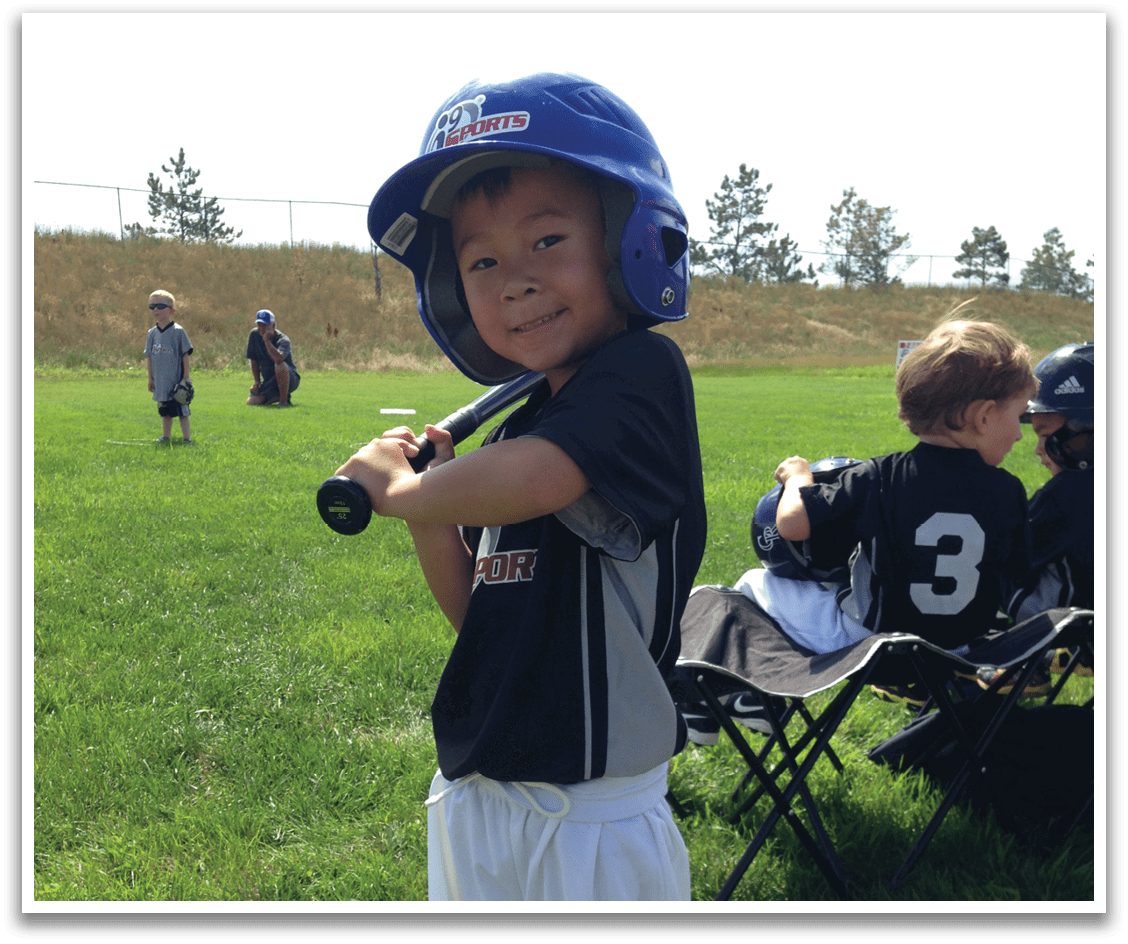 A young boy is standing in a grassy field, holding a baseball bat. AI generated content