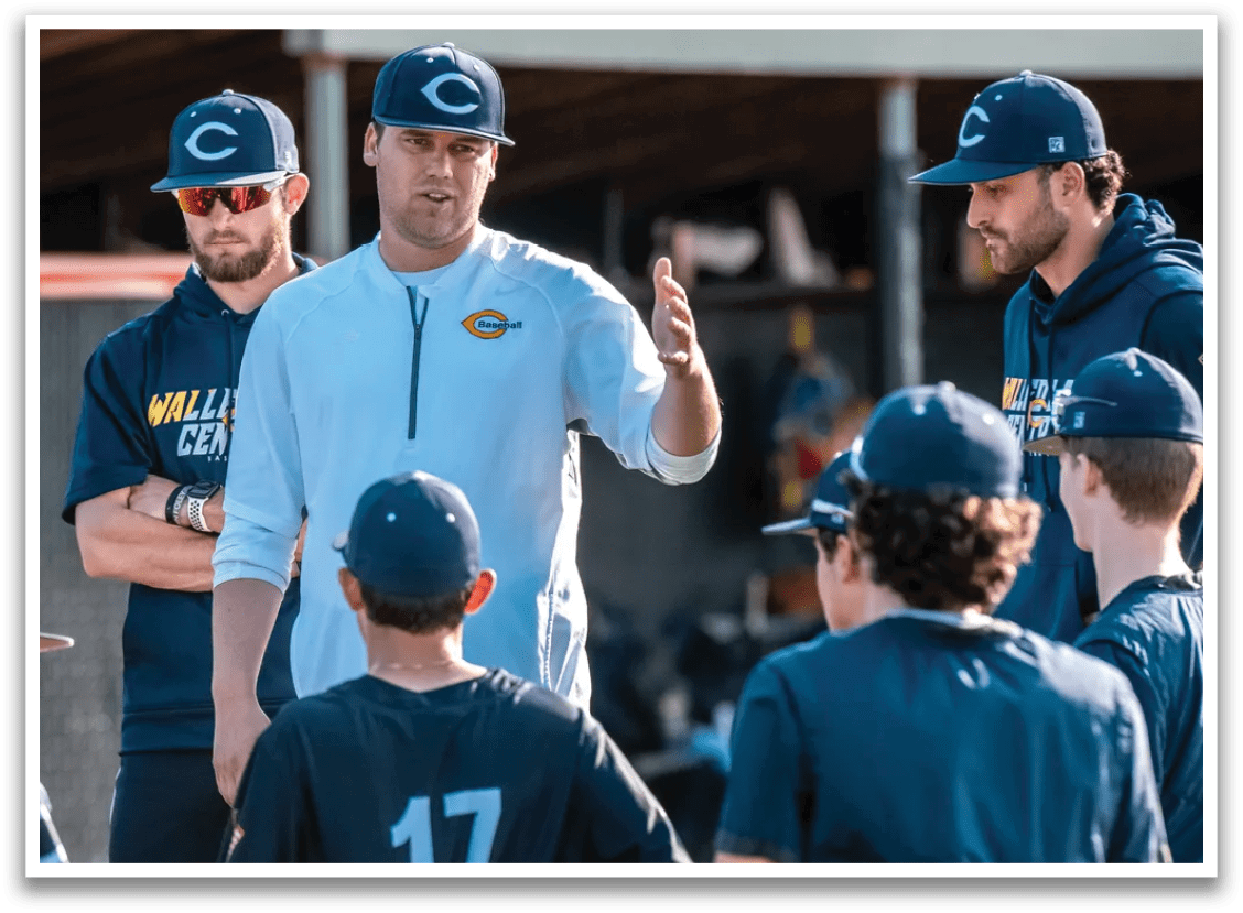 A group of baseball players wearing blue and white uniforms are gathered around a man in a white shirt. The man is talking to the players, possibly giving instructions or discussing the game. The players are listening attentively, with some of them wearing baseball gloves. AI generated content