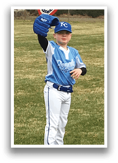 A young boy in a blue shirt and white pants is standing on a grassy field, holding a baseball glove. AI generated content