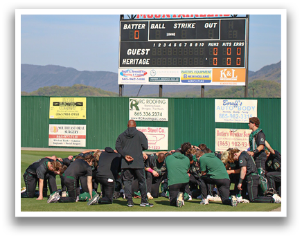 A group of people are huddled together on a field, with some of them kneeling. They are facing a scoreboard, which is displaying the score of a baseball game. AI generated content