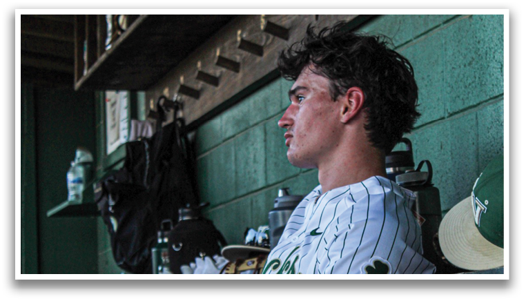 A baseball player sits on a bench with his legs crossed, wearing a baseball uniform and a green hat. There are several baseball bats and gloves around him, as well as a bottle and a cup. AI generated content