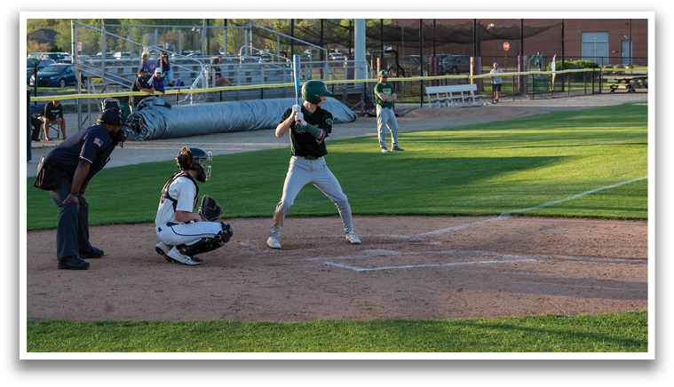 A baseball game is in progress with a batter swinging a bat, a catcher ready to catch the ball, and an umpire behind them. There are several other people in the scene, some of whom are standing and others sitting on chairs. A bench is also visible in the background. AI generated content