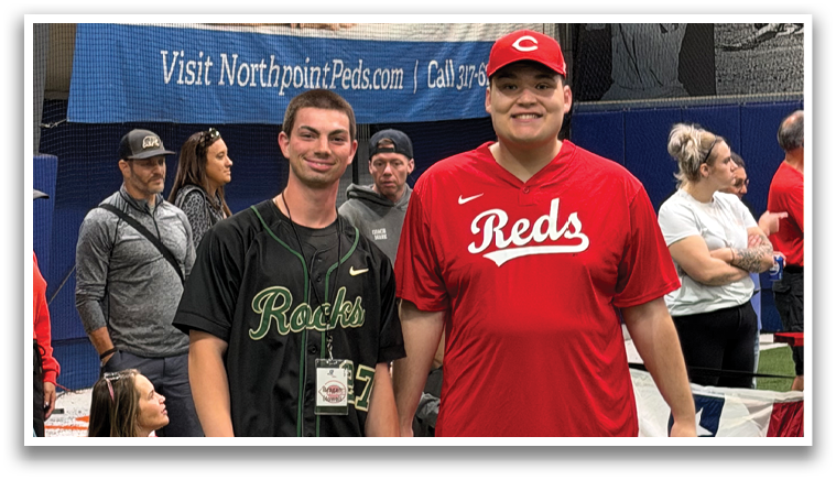 Two men in red shirts are standing on a baseball field, one holding a baseball glove. They are surrounded by a group of people, including a young boy. AI generated content
