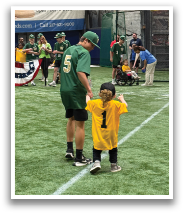 A man and a boy are standing on a baseball field, both wearing baseball uniforms. The boy is wearing a yellow jersey and a green hat. The man is standing behind the boy, possibly coaching him. There are several other people in the background, some of whom are also wearing baseball uniforms. A baseball bat can be seen in the scene, indicating that they are practicing or playing baseball. AI generated content