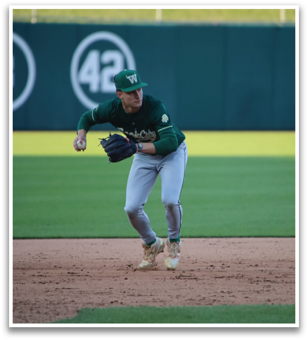 A baseball player wearing a green shirt and white pants is running on the field. Description generated by AI
