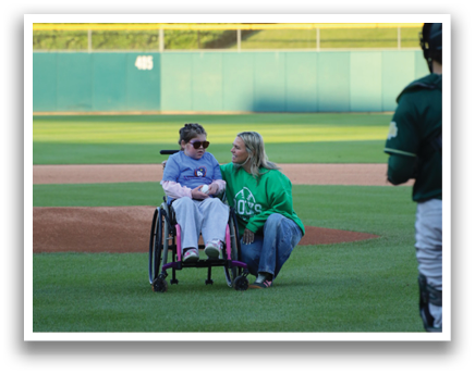 A man in a wheelchair and a woman in a green shirt sit on the field. Description generated by AI