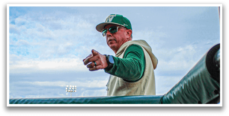 A man wearing a green hat and white shirt is standing on a baseball field. Description generated by AI