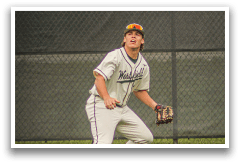 A baseball player in a white uniform and a brown hat is standing on a grass field. Description generated by AI