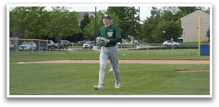 A baseball player wearing a green and white uniform is sitting on the ground with a catcher's mitt on his left hand. Description generated by AI