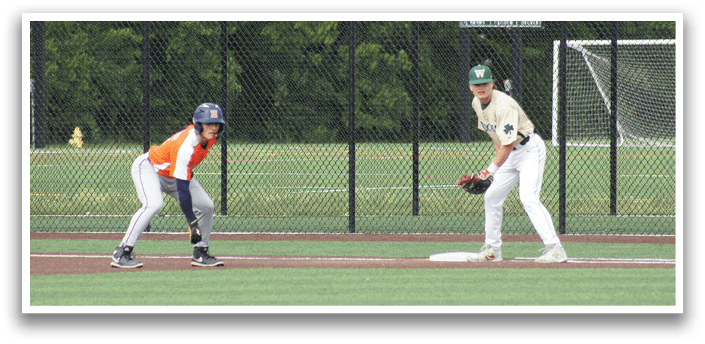 A baseball player wearing a green and white uniform is sitting on the ground with a catcher's mitt on his left hand. Description generated by AI