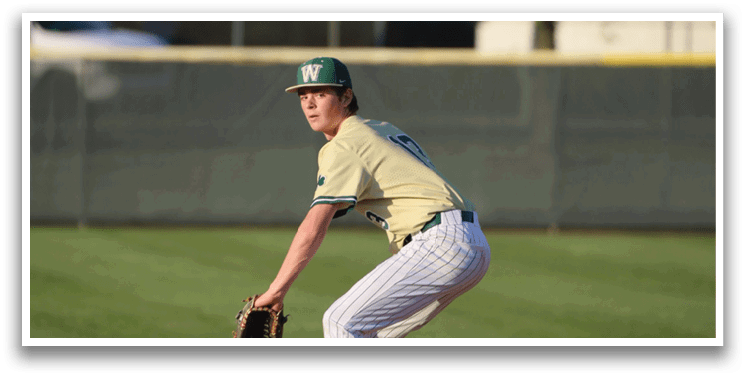 A man wearing a green hat and white shirt is standing on a baseball field. Description generated by AI