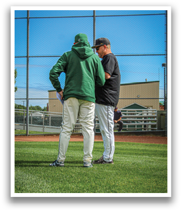 Two men wearing baseball uniforms standing on a grassy field. Description generated by AI