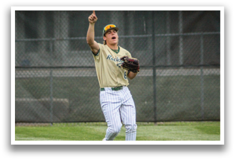 A baseball player in a gold and green uniform is holding a glove and pointing upwards. Description generated by AI