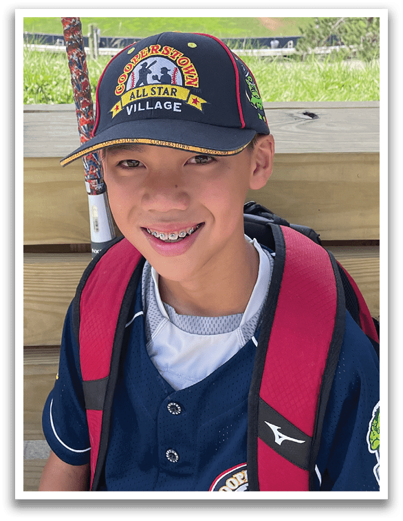 A young boy wearing a blue baseball jersey and a red backpack. Description generated by AI