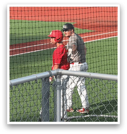 A baseball field with a fence and a man in a red hat. Description generated by AI