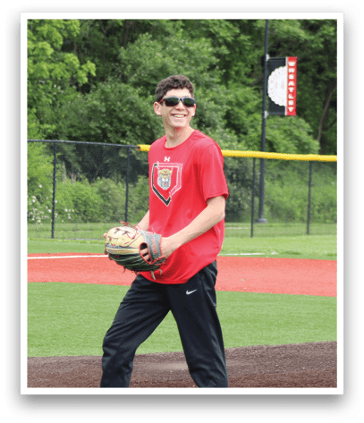 A boy wearing a red shirt and black pants is standing on a baseball field. Description generated by AI
