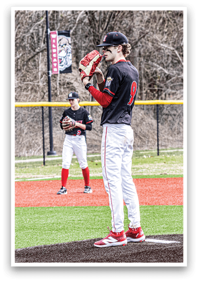 A baseball player in a black shirt and red shoes is standing on the pitcher's mound. Description generated by AI