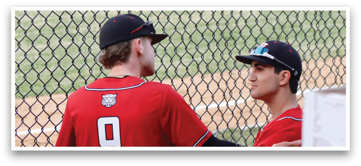 Two baseball players wearing red shirts and white pants. Description generated by AI