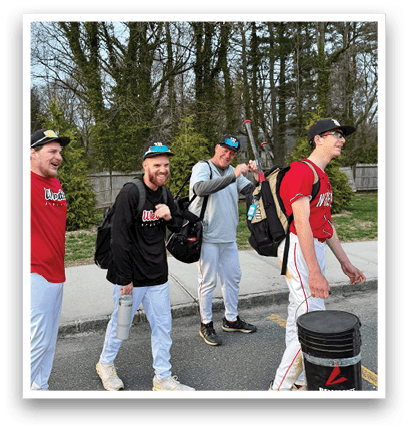 Three men wearing baseball uniforms and hats are walking down a sidewalk. Description generated by AI